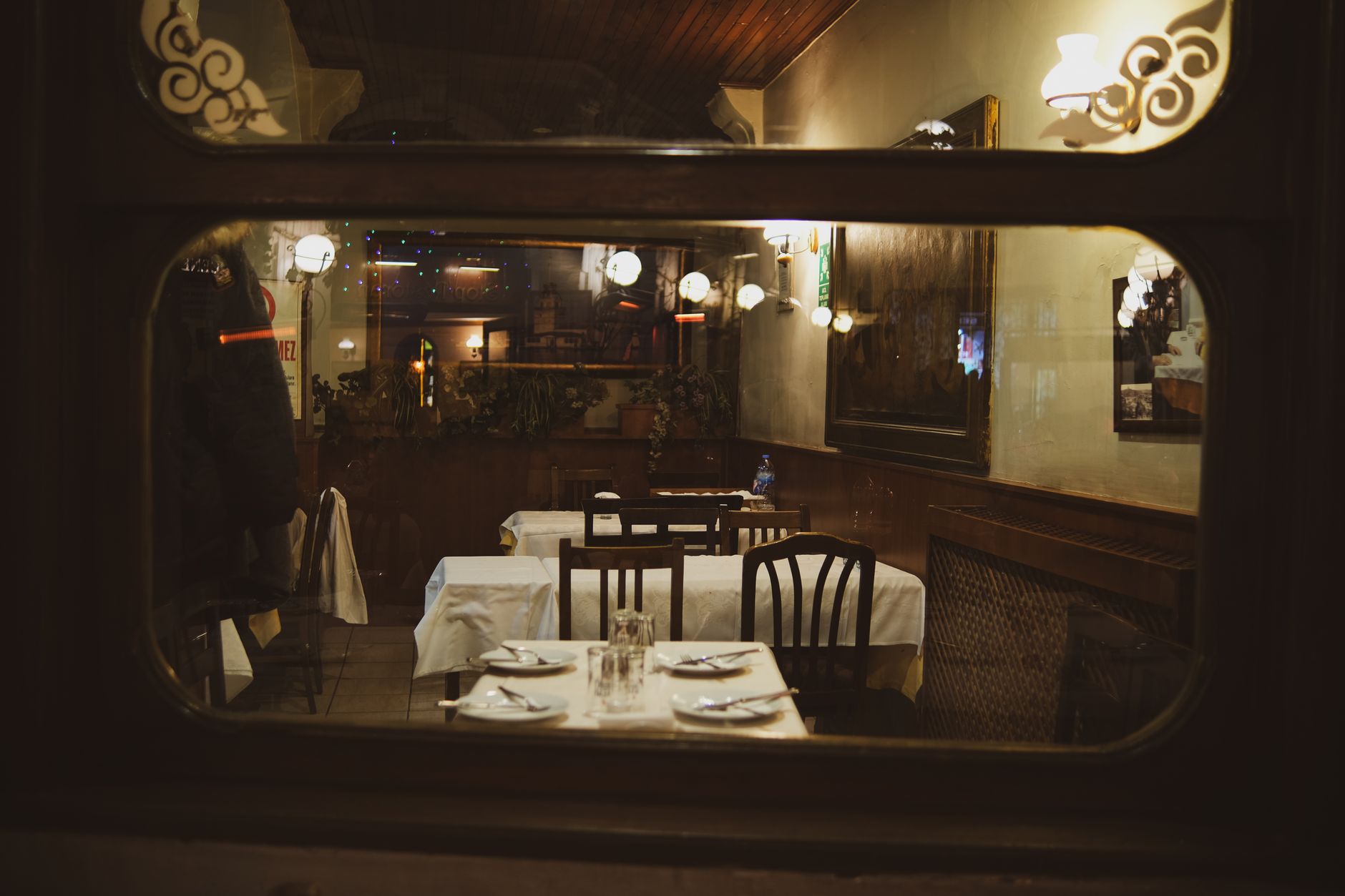 Gece penceresinden salon: örtülü masalar, ahşap sandalyeler