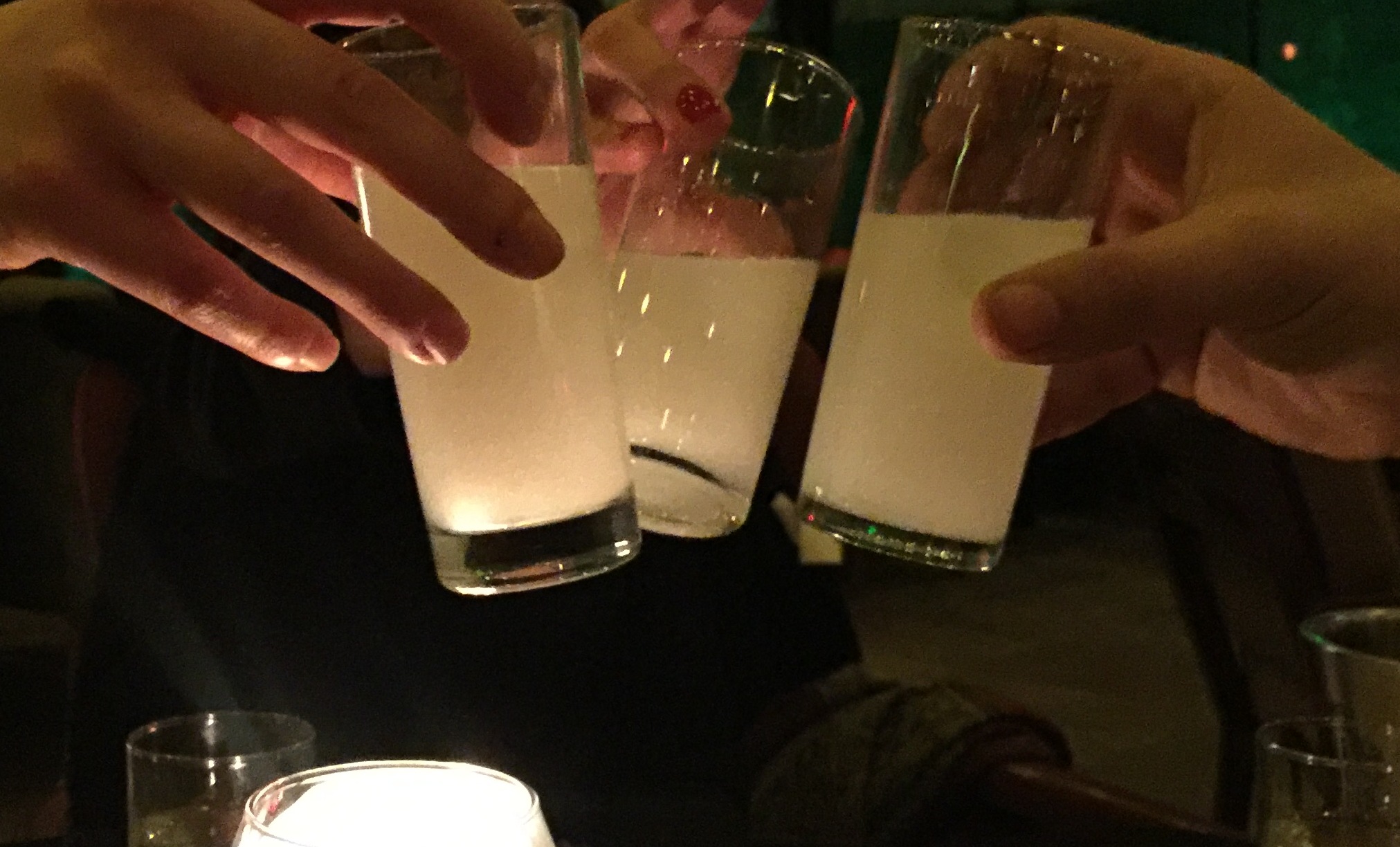 Loş salonda mum ışığında tokuşturulan üç rakı kadehi; buzla beyazlaşmış rakı, altta su bardakları